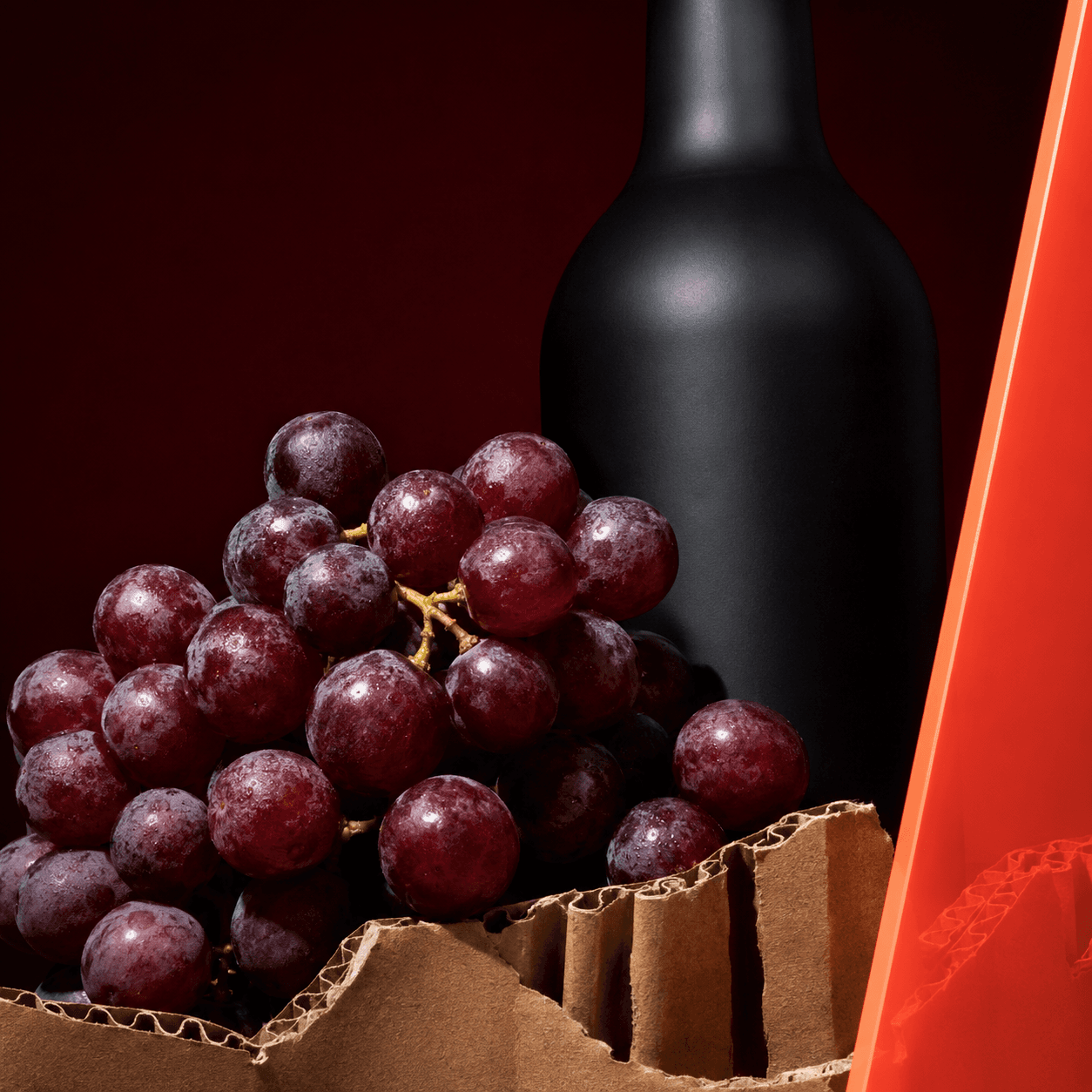 Red grapes, a black wine bottle, and a corrugated wine case